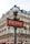 A classic Parisian metro sign with art deco design stands in front of a traditional Haussmann-style building. The sign is red with white letters, and it is topped with an ornate street lamp. The building in the background features multiple windows and wrought-iron balconies.