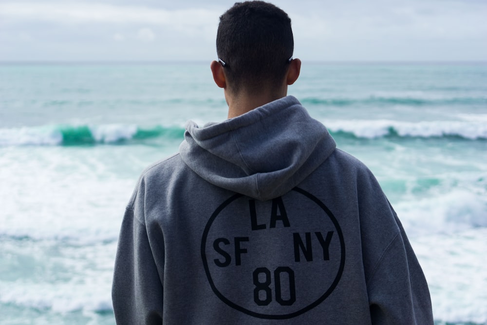 man wearing grey pullover hoodie standing on shore overlooking body of water during daytime