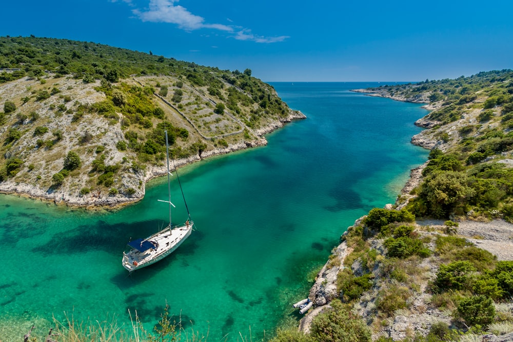 fotografia aerea della barca bianca vicino allo specchio d'acqua tra la montagna verde durante il giorno