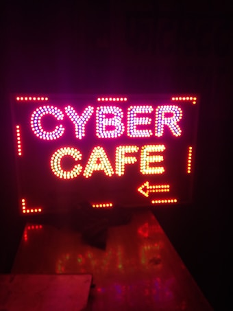 Brightly lit sign displaying the words 'CYBER CAFE' with an arrow pointing to the right, using colorful LED lights against a dark background.