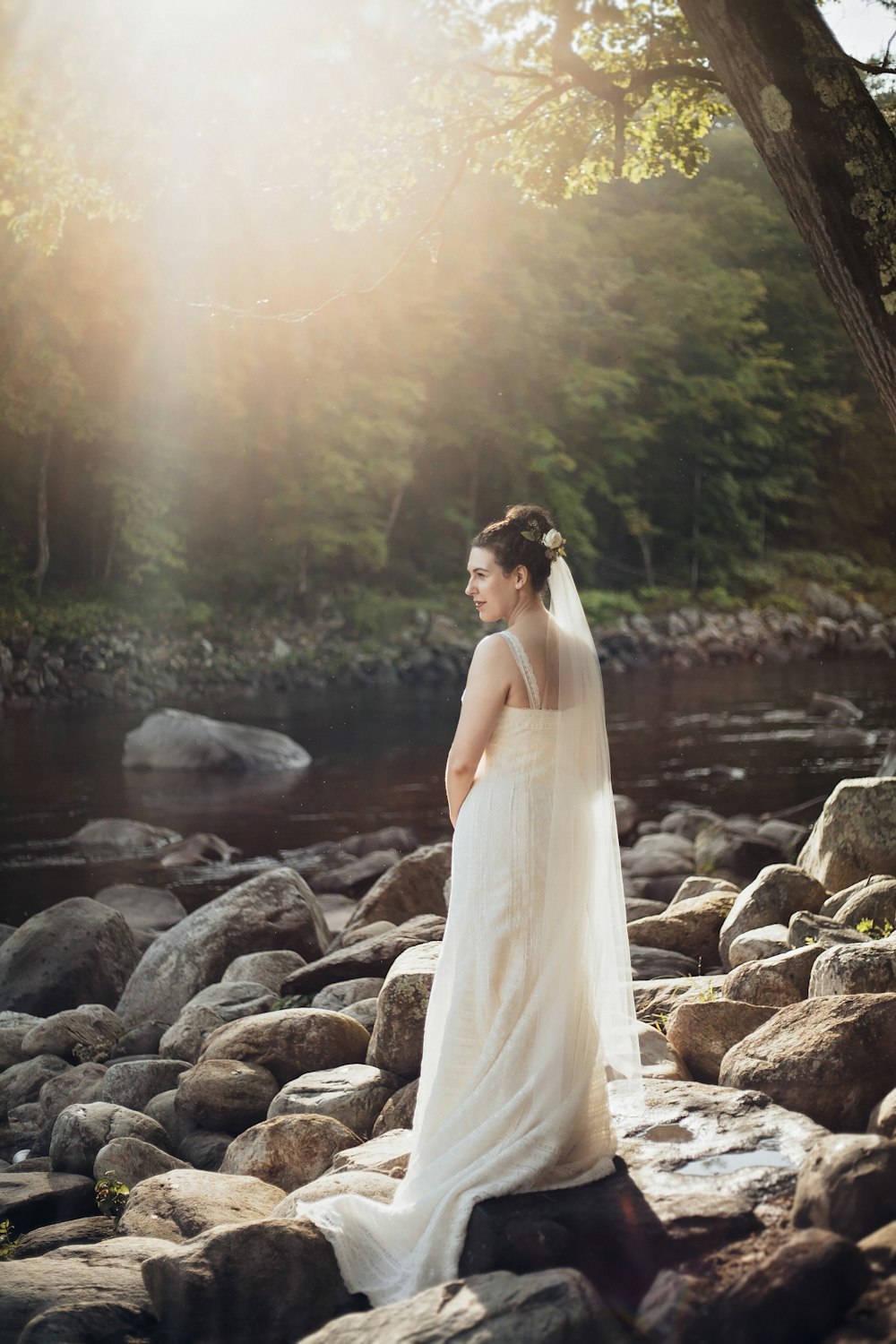 woman standing on gray rock near lake during sunset