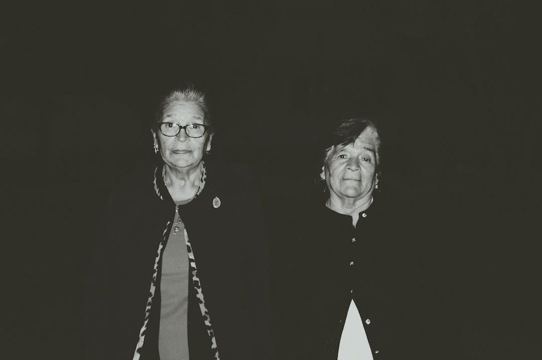 Two older women looking at the camera, with a black background.