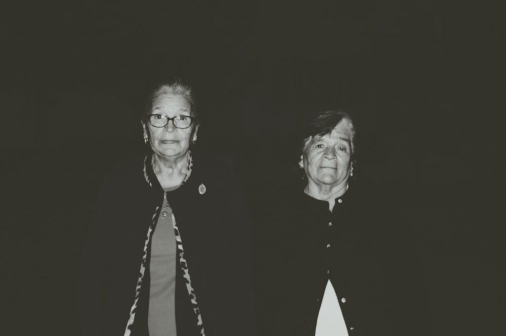Two older women looking at the camera, with a black background.