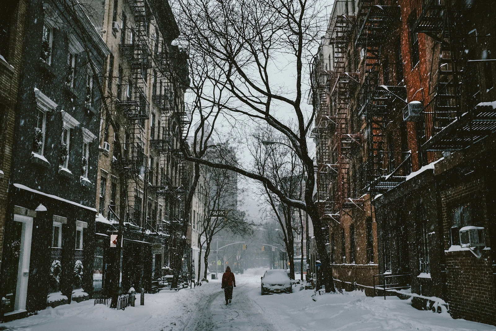 Travel photograph: A lone person walking along a snow-covered West Village street beneath bare trees and fire escapes.