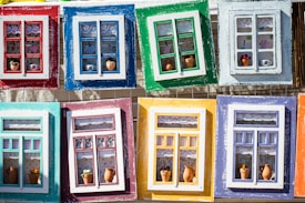 Colorful and artistic window frames arranged in a grid, each frame features a unique design with different arrangements of lace curtains, miniature pots, and decorative items.