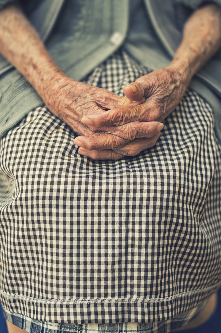 An elderly person's folded hands resting in their lap