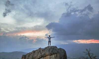 man standing on top of rock mountain during golden hour