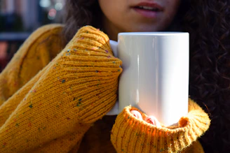 A vibrant hand-thrown ceramic mug in sunny yellow with a cozy knitted scarf beside it.
