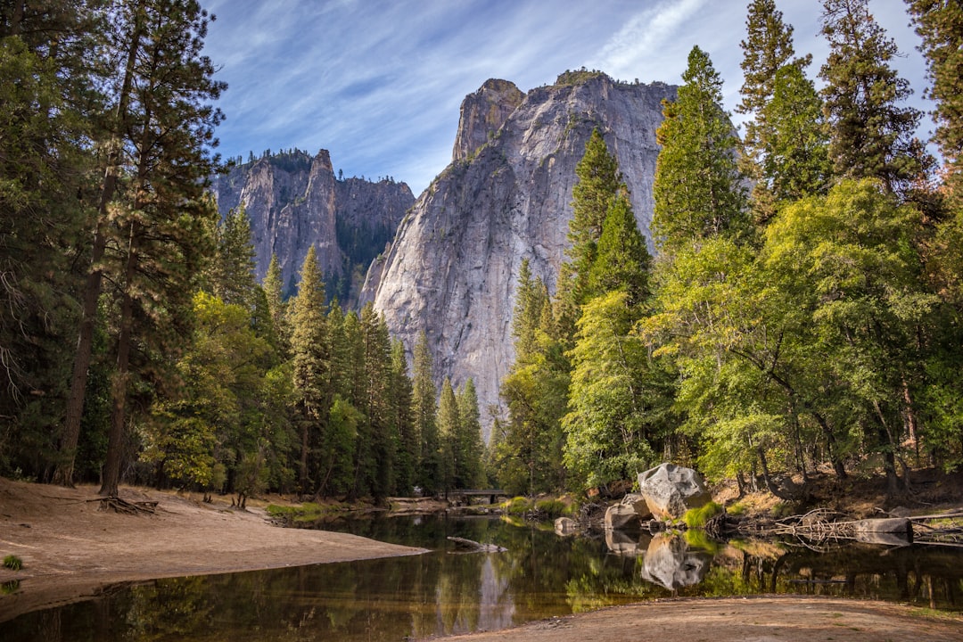 calm body of water surrounded by trees near cliff, River beneath Yosemite cliffs