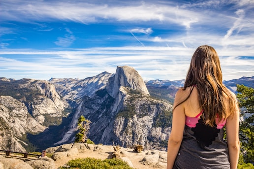 A young woman standing confidently on a mountain peak, overlooking a vast landscape at sunrise.