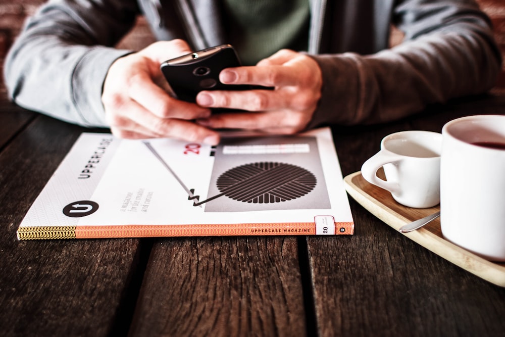 pessoa segurando o smartphone Android preto enquanto se inclina na mesa