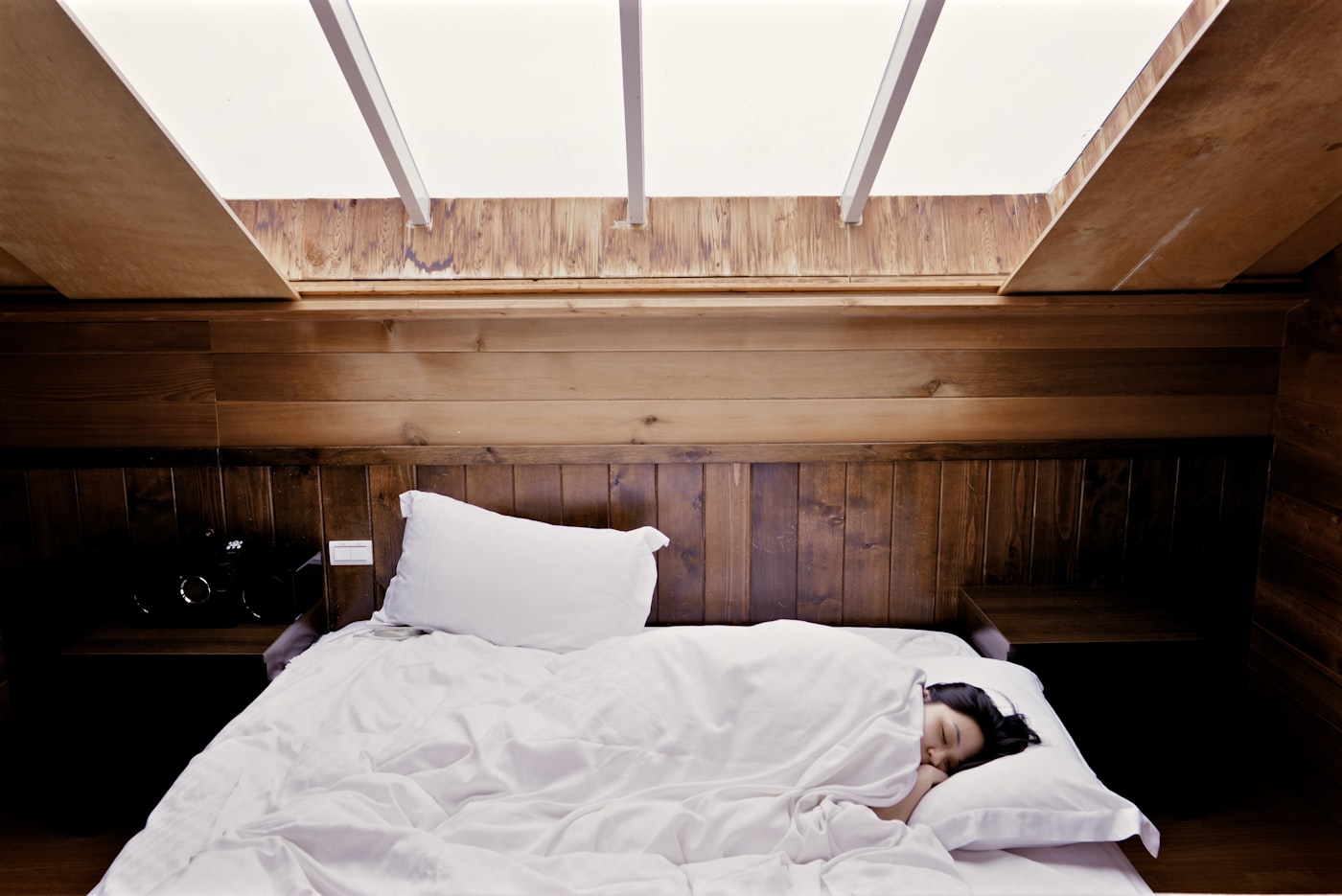 Woman asleep in a bed under a soft skylight
