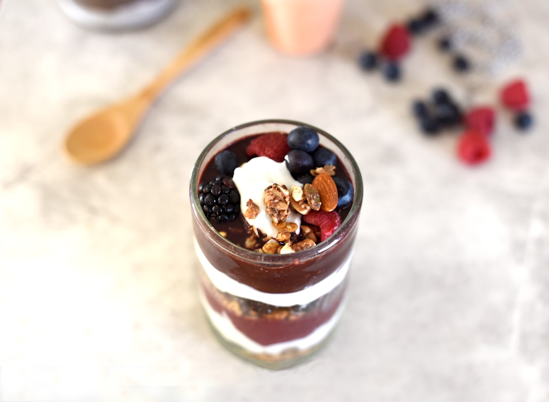 A glass filled with cake, pudding, cream, fruit, berries, and nuts
