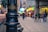 A bustling urban street scene with a black metal post in the foreground labeled 'Monterrey Historico'. In the background, people are walking along a pedestrian area lined with various storefronts featuring neon lights and signs. The atmosphere appears lively and busy.