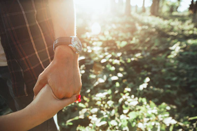 Close-up of hands exchanging overlanding gear in a sunlit forest clearing.