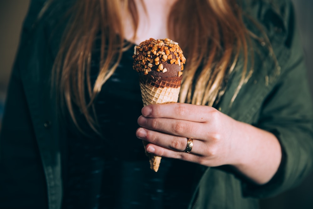 Femme en veste verte tenant de la crème glacée au chocolat enduite de noix pendant la photographie de mise au point peu profonde de jour