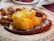 A plate of grilled octopus tentacles paired with large pieces of boiled potatoes, seasoned with red paprika or chili powder. The dish is presented on a decorated ceramic plate, suggesting a Mediterranean or Spanish style cuisine.