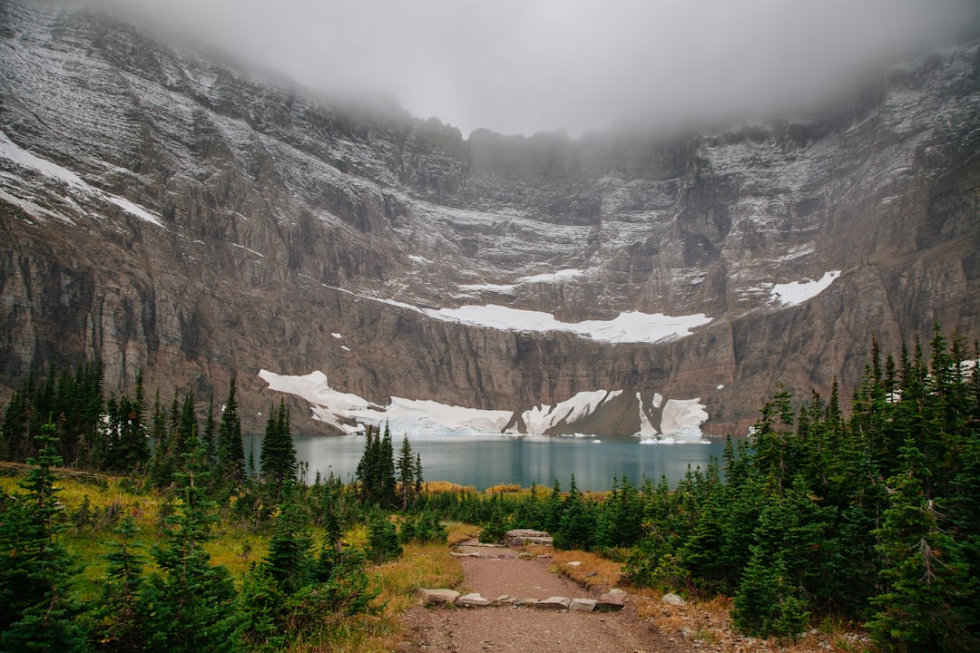 Fog circling above snowy mountains leading down to Iceberg lake surrounded by trees