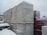 Large pallets covered in plastic wrap are stacked outdoors, all covered with a layer of snow. The scene is set against an overcast sky, suggesting a cold and snowy environment. The ground is not visible, likely under snow, and the pallets appear to be in an industrial or storage area.