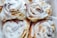 Four cinnamon rolls with a generous coating of white icing are grouped together. The rolls have a slightly golden-brown color and are nestled closely, filling the frame.