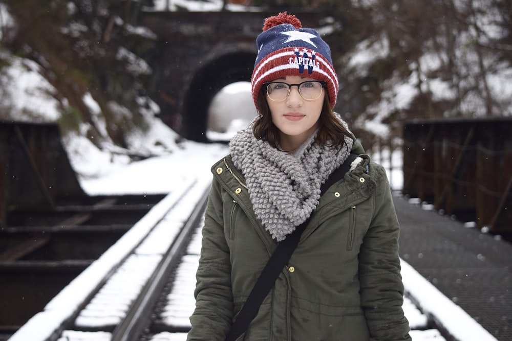 woman in green coat carrying black sling bag standing on railway