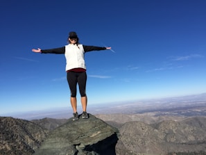 A person standing on a cliff edge, arms wide open embracing the sky.
