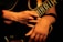 A close-up view of a person's hands skillfully playing an electric guitar. The lighting creates dramatic shadows and highlights the contours of the hands and the guitar strings.