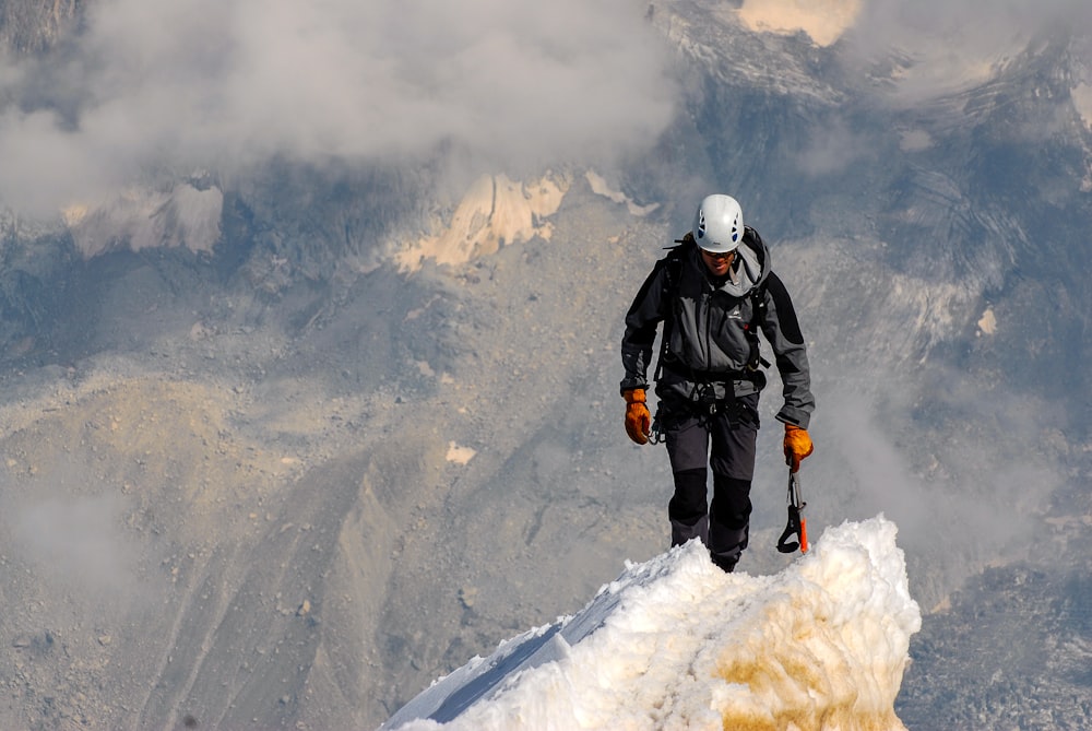 One climber making it to the top surrounded by clouds and snowy mountains