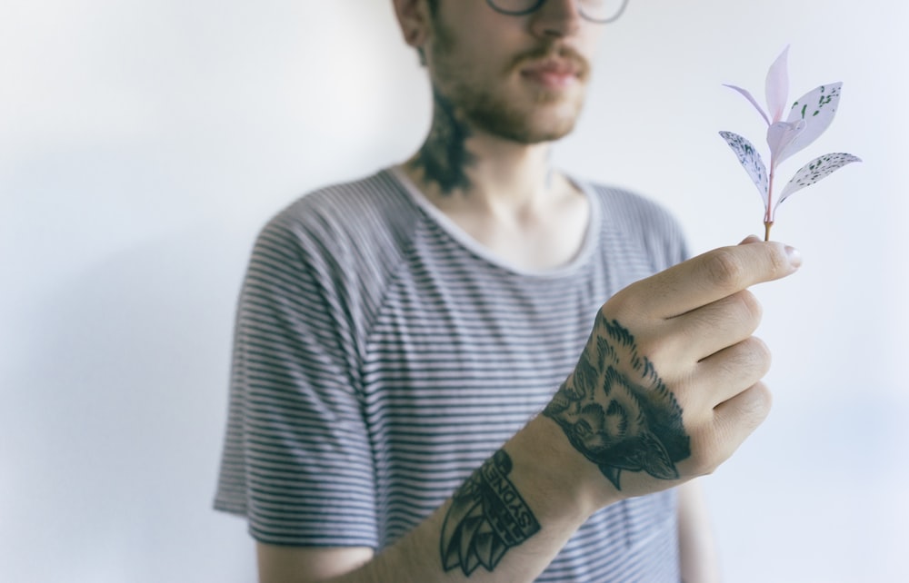 man wearing shirt holding white leafed plant