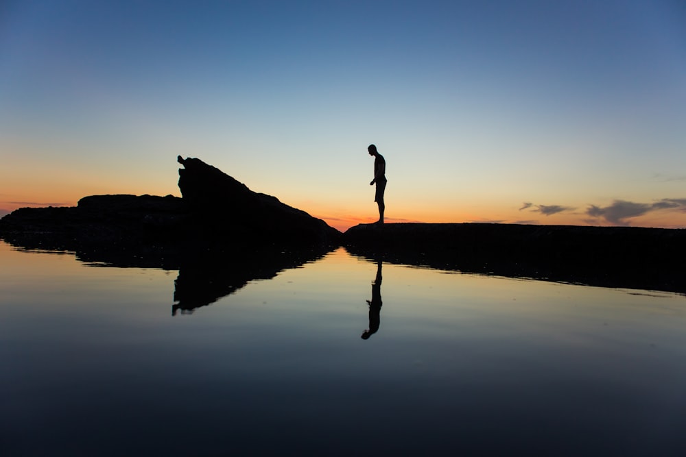 silhouette of man standing on land near body of water with reflection