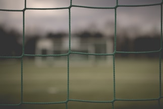 Close-up of green sports netting stretched tightly on a soccer field under bright sunlight