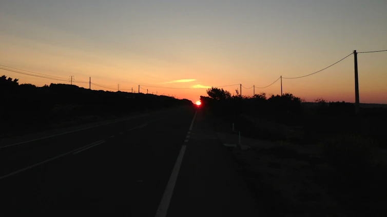A sleek, freshly paved highway stretching under a golden sunset, showcasing smooth asphalt and neatly arranged interlocking pavers on the sidewalk.