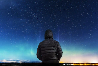A sleek black jacket with glowing blue constellation patterns under a starry night sky.