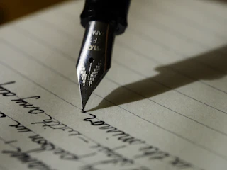 Silver Pilot fountain-pen nib touching cream ruled paper with a wet black ink dot