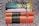 A stack of books on a patterned fabric background, topped with a string of black and white prayer beads. The titles include 'The Secret Lives of Baba Segi's Wives' and 'Half of a Yellow Sun', along with collections referred to as 'The African Trilogy' and 'The Cairo Trilogy'.