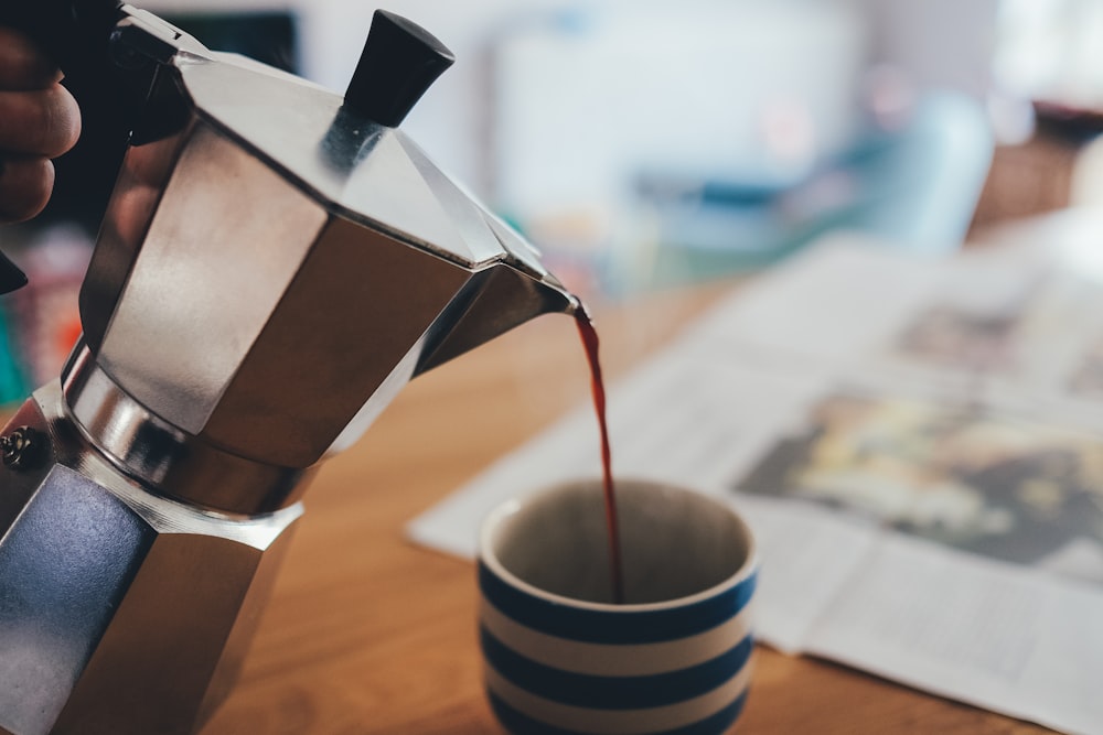 théière turque en argent versant un liquide brun dans une tasse en céramique rayée blanche et bleue