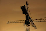 A sunset silhouette of a crane lifting materials, casting shadows over a violetforge project.