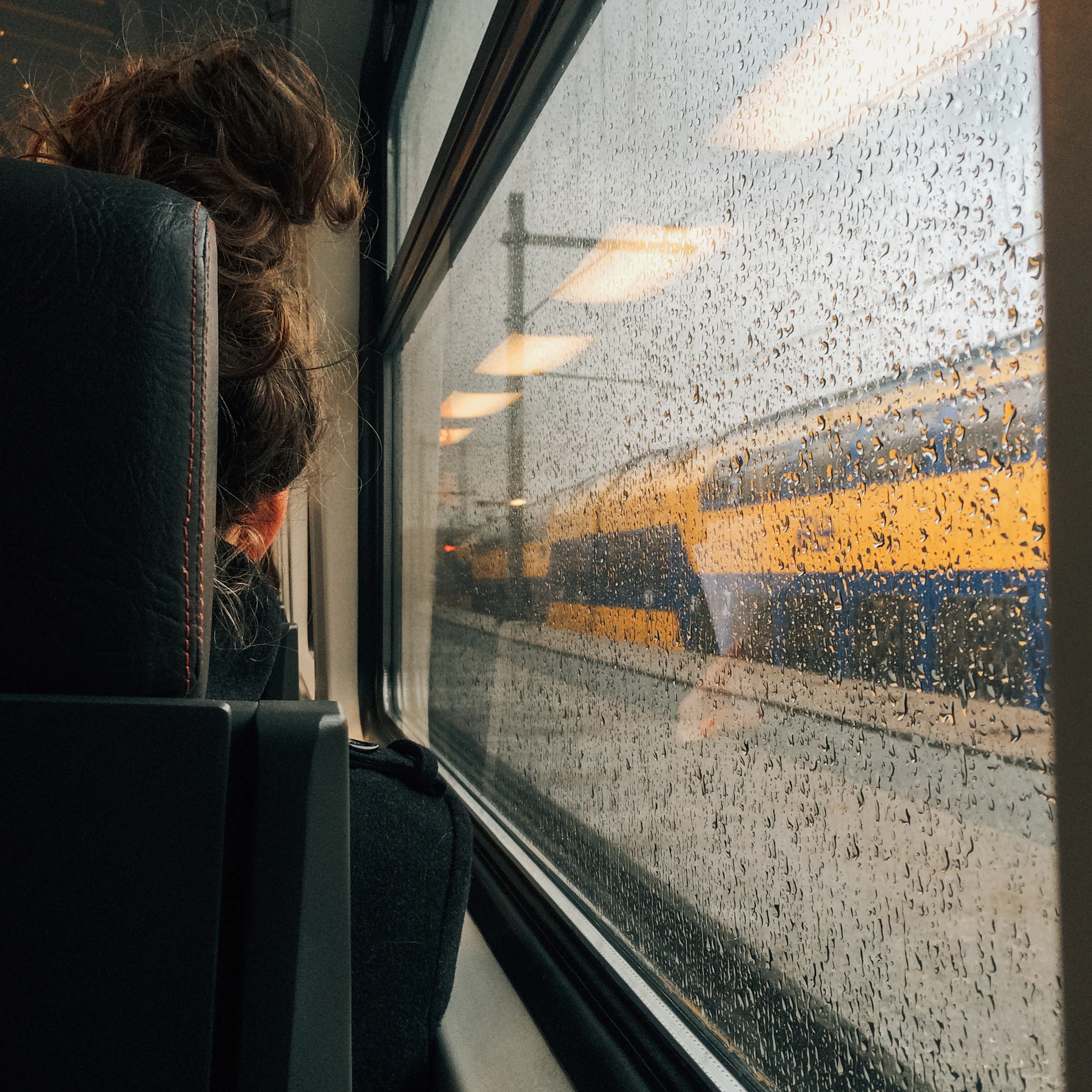 A traveler looks through a rainy train window.