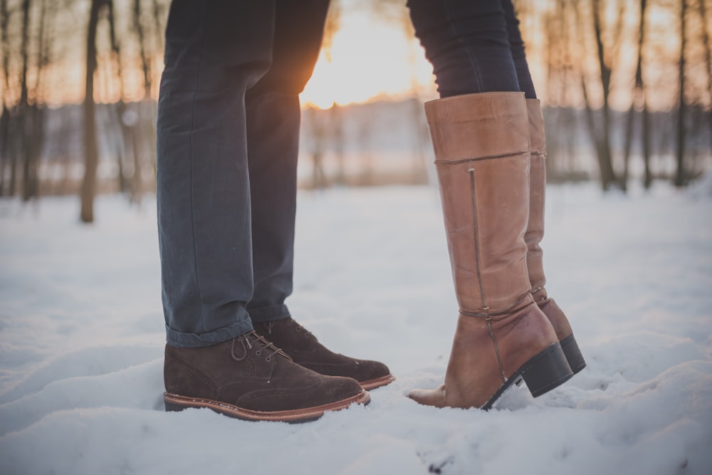 duas pessoas em botas marrons e sapatos na floresta nevada