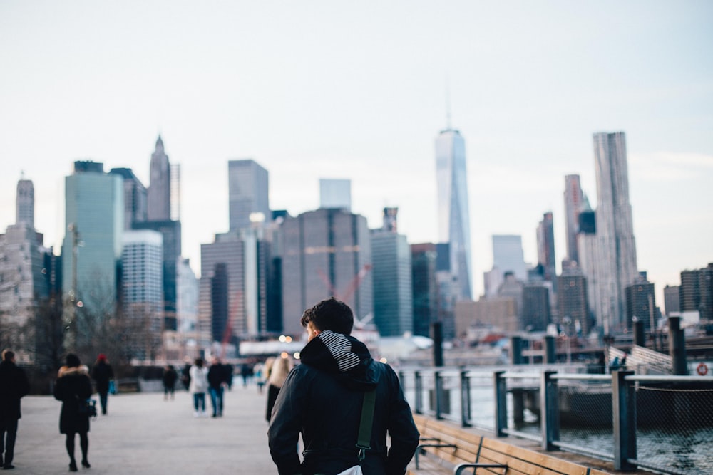 selective focus photography of man standing near body of water walking towards buildings