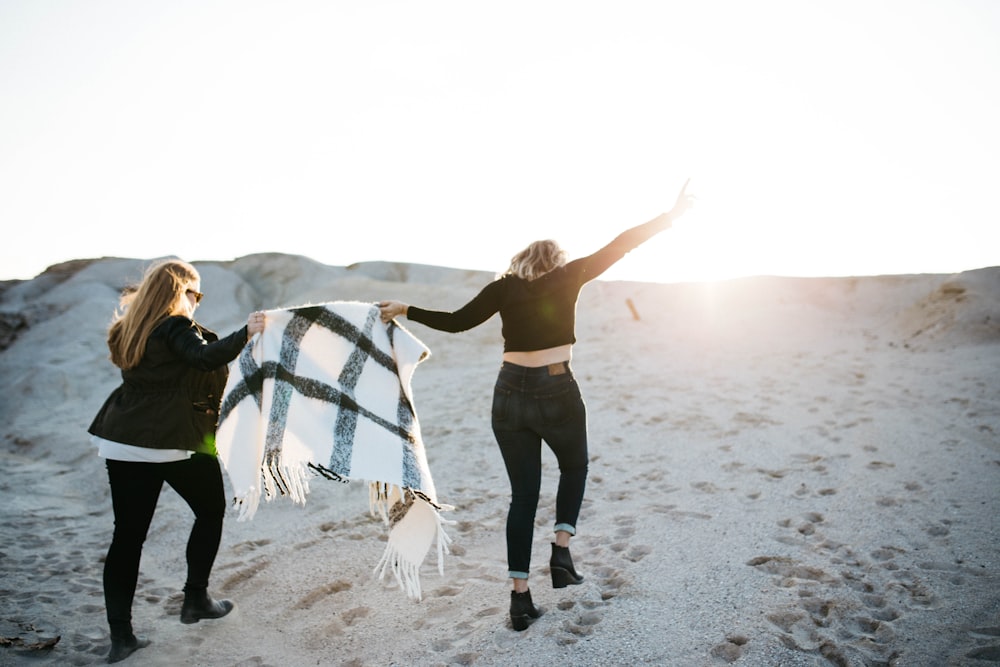 vignette photography of two woman holding scarf walking on sand