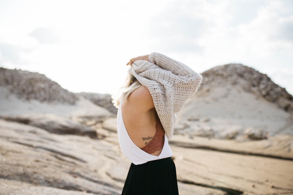 woman about to wear beige knit sweater under white cloudy sky