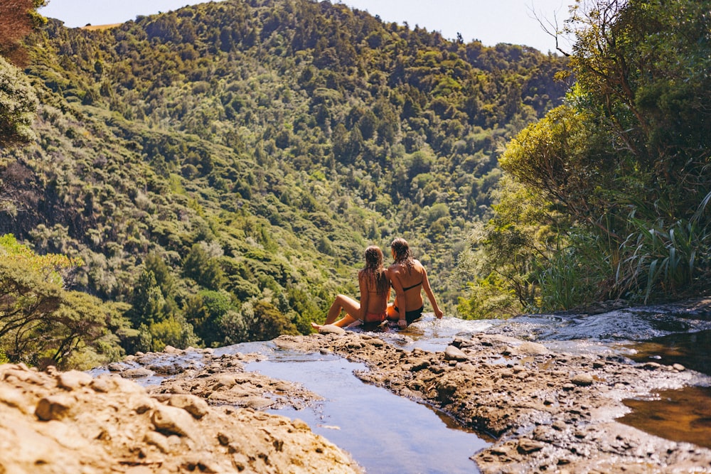 two women sitting on stream leading to mountain