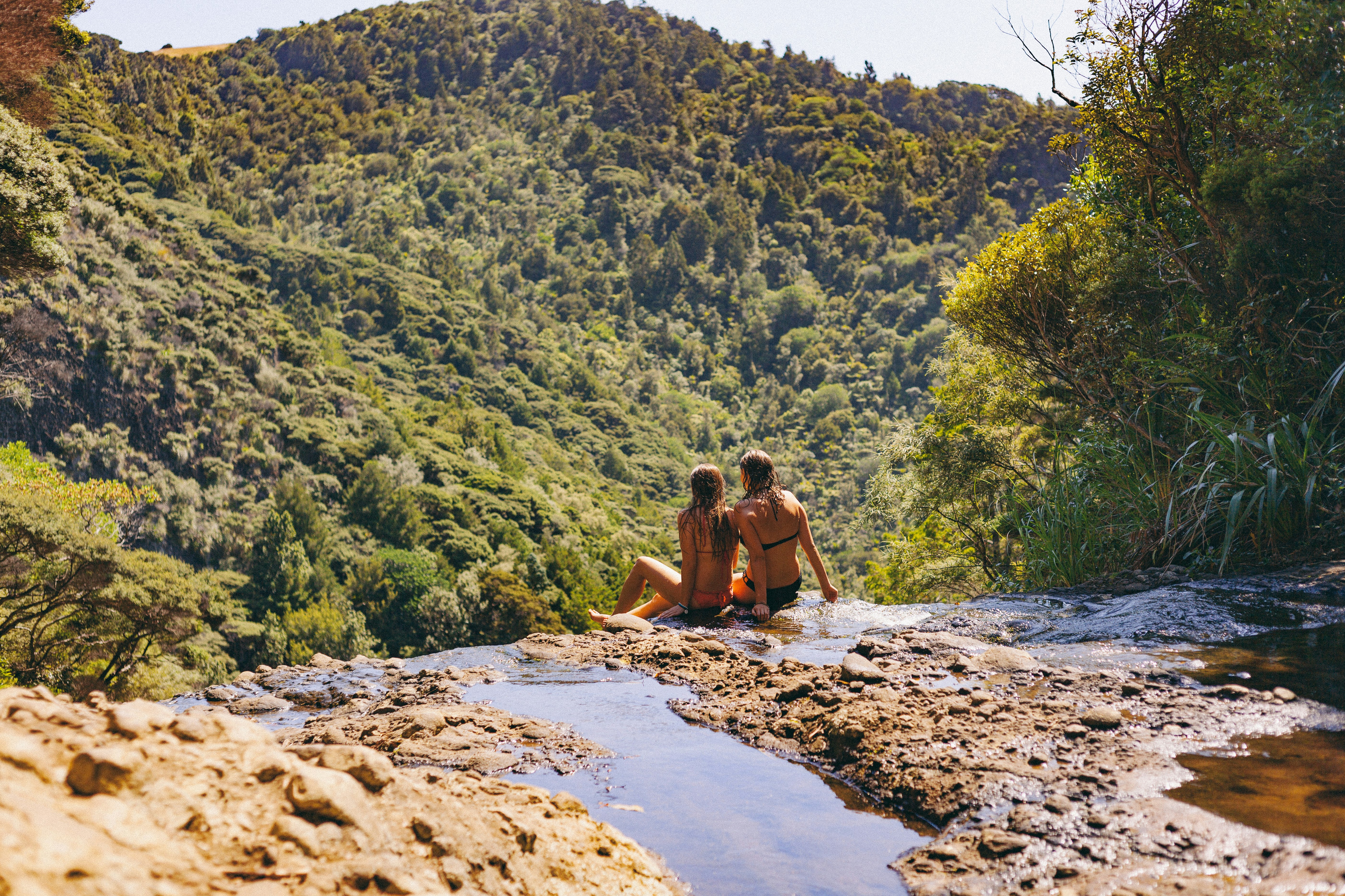 two women sitting on stream leading to mountain