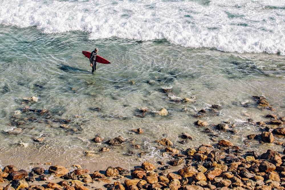 personas que sostienen una tabla de surf roja de pie en el cuerpo de agua