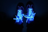 Close-up of electric cyan sneakers glowing against a deep near-black background.