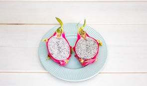 2-sliced dragon fruit in ceramic plate placed on wood plank