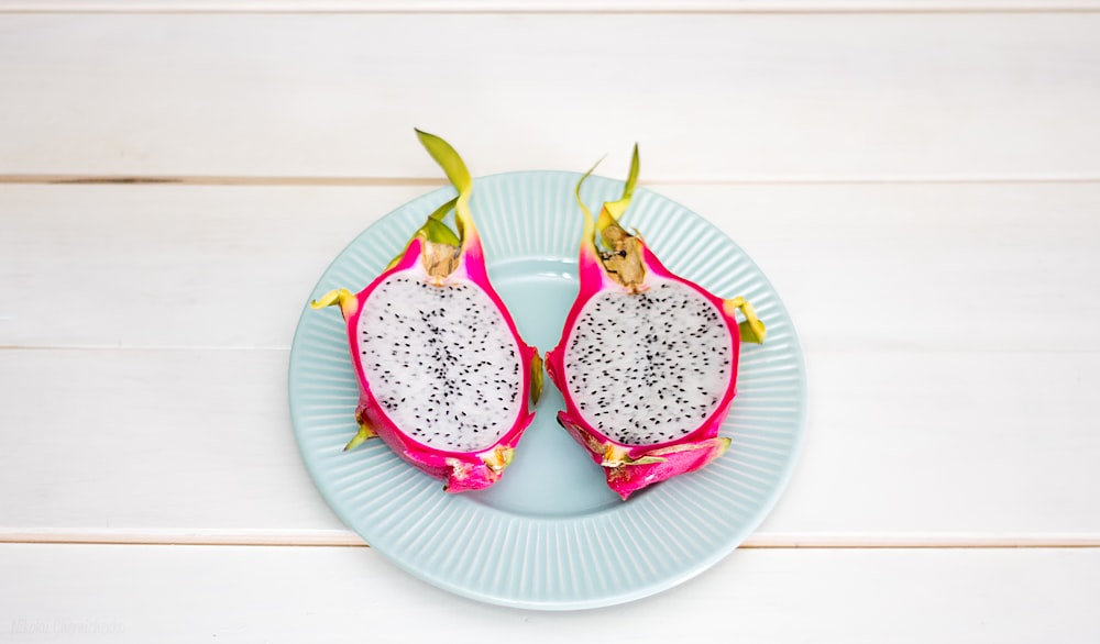 2-sliced dragon fruit in ceramic plate placed on wood plank