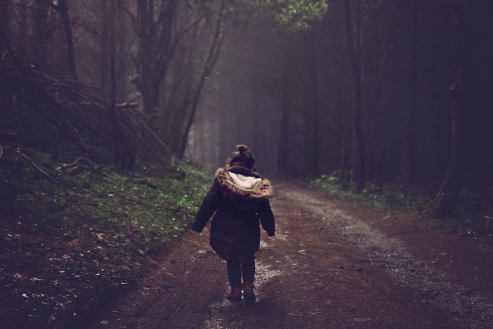 昼間の森の中を歩く茶色のパーカージャケットの女の子