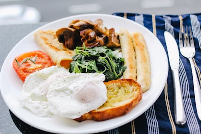 sunny side-up egg on white ceramic plate beside stainless steel butter knife and fork breakfast zoom background